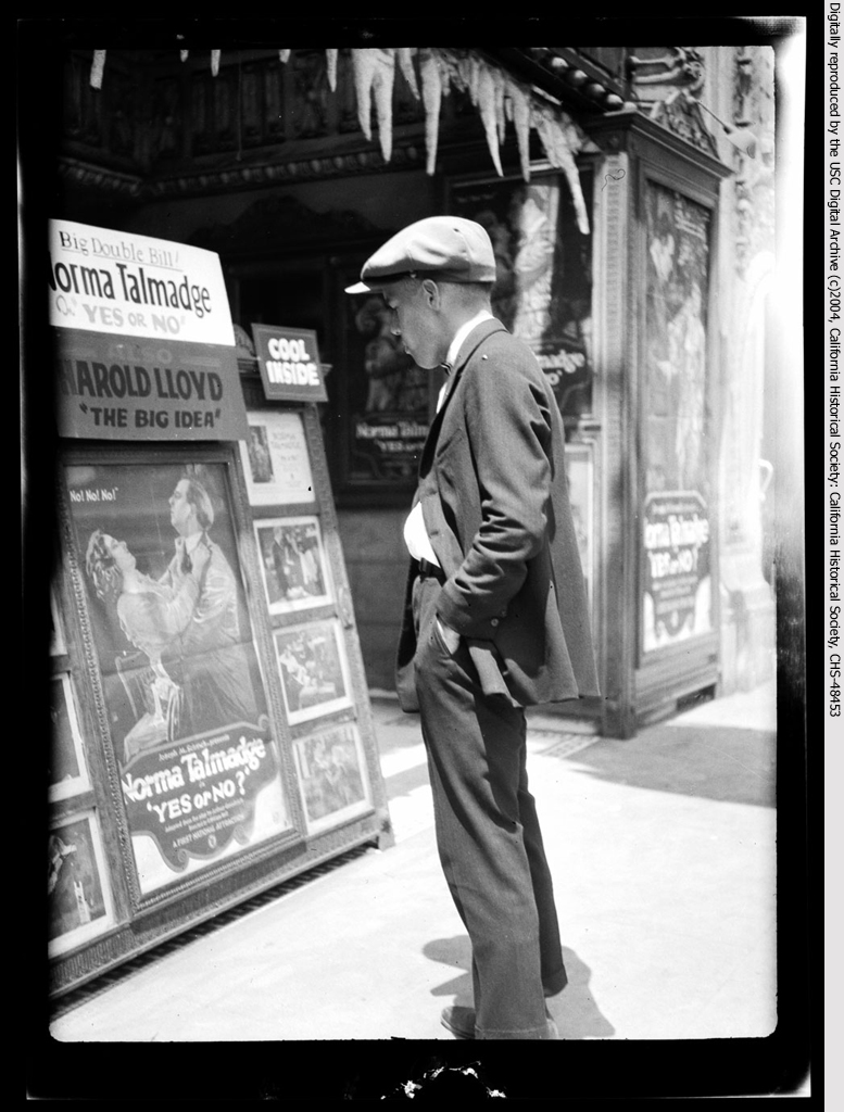 Man standing outside a movie theater looking at posters, ca.1920.jpg