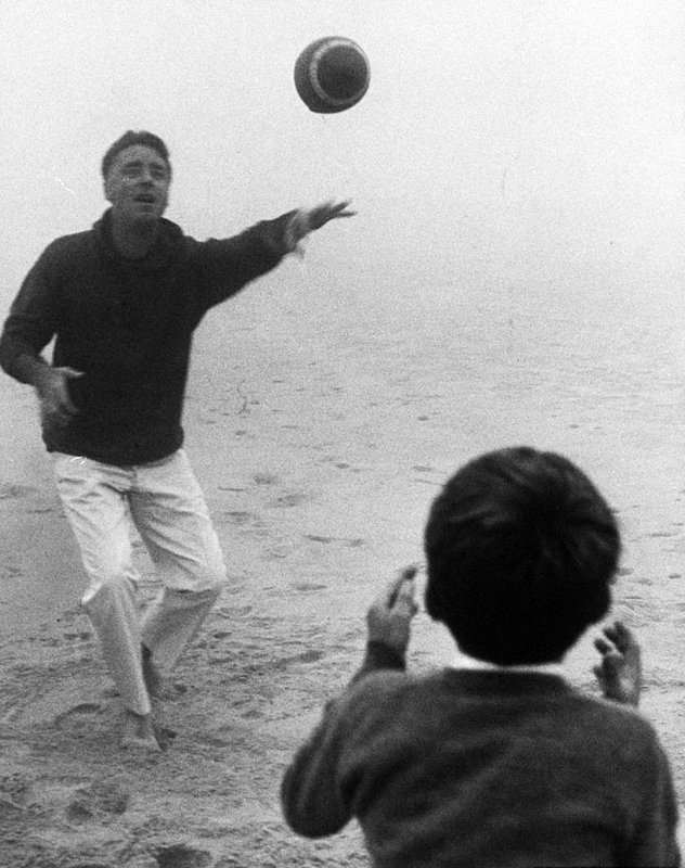 Actor Peter Lawford playing football on beach with his son..jpg