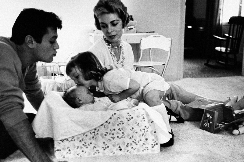 Actor Tony Curtis and actress wife Janet Leigh watching as daughter Kelly kisses infant sister Jamie Leigh in the girls