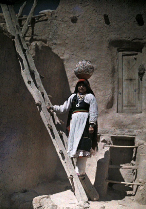 New-Mexico-Water-carrier-stands-on-ladder-in-Acoma-pueblo-balancing-jug-on-head.jpg